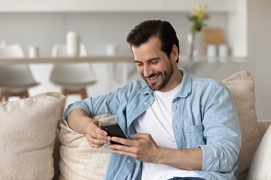 man smiling using his phone while sitting on the couch