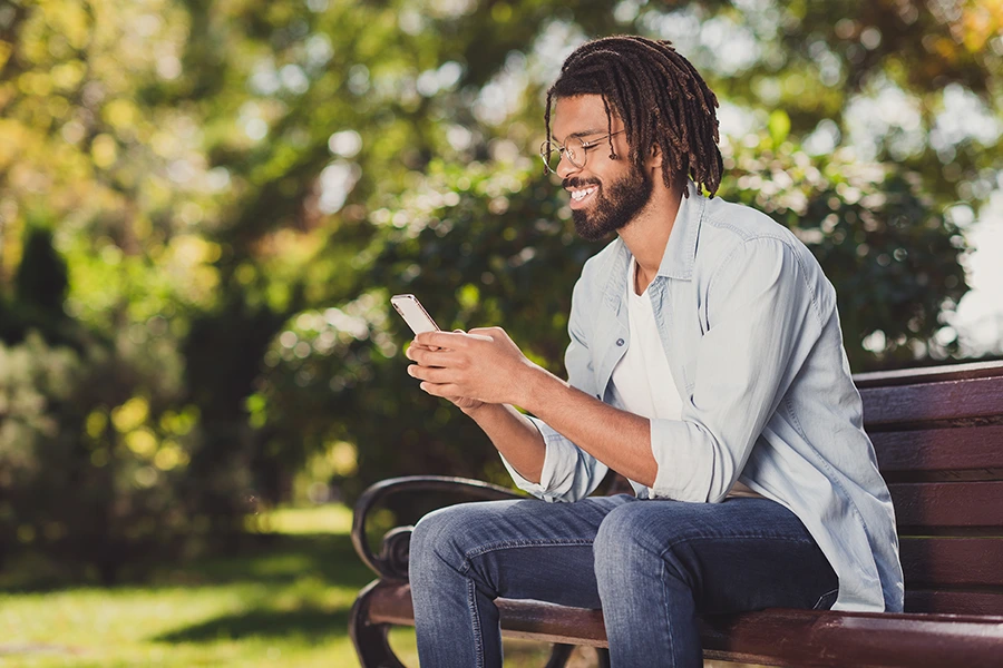 man using phone while sitting on a bench in a park